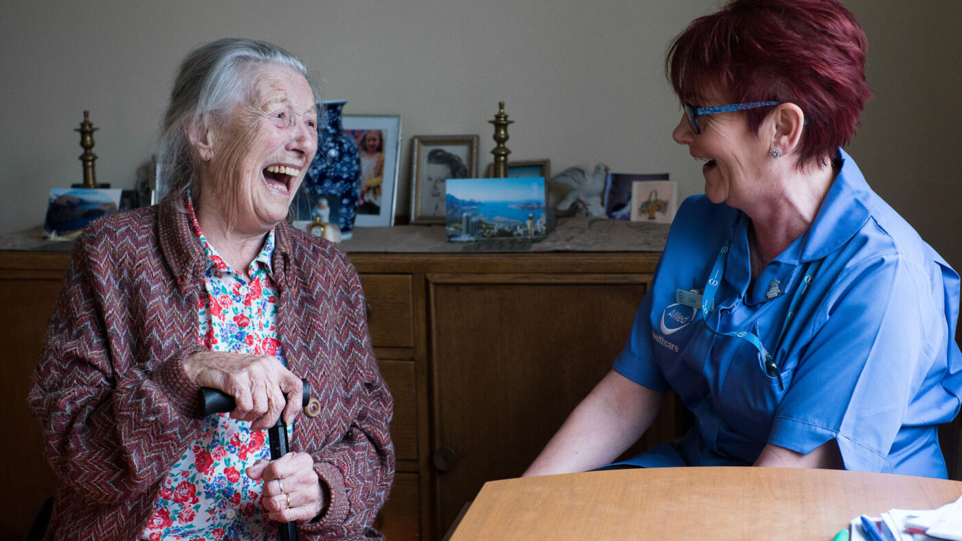 A carer and an an elderly lady laugh together